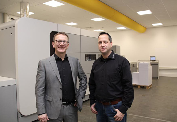 Torsten Bischof (links), Geschäftsführer documenteam und Kai Becker, Vertriebsleiter documenteam vor der neuen Farb-Digitaldruckmaschine, die 300 DIN-A4-Seiten pro Minute produzieren kann. (Foto: documenteam GmbH & Co. KG)