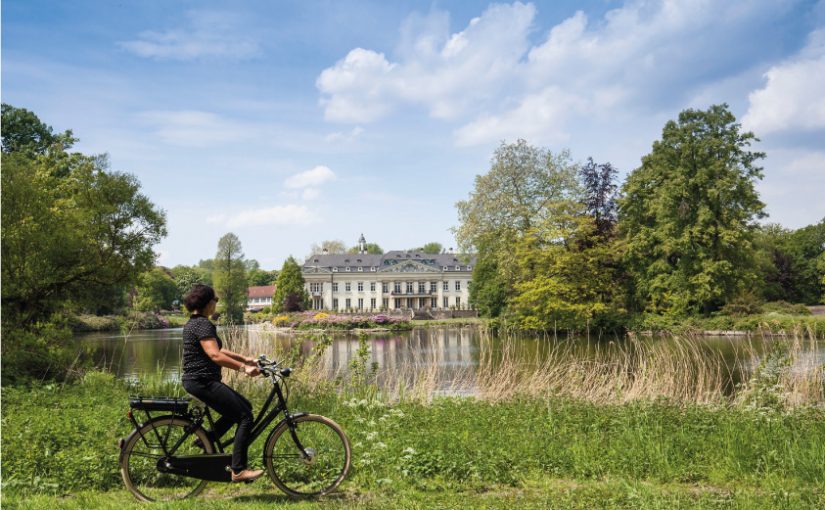 Mit Abstand unterwegs: Auf der 100 Schlösser Route winken imposante Bauwerke von nah und fern, wie hier das Schloss Varlar. Fahrradfahrerin vor Schloss Varlar © Münsterland e.V./Hans Zaglitsch