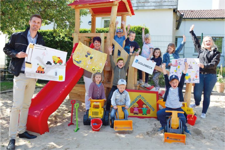 Einen kleinen Fuhrpark knallgelber Baufahrzeuge übergaben Maik Becker, Vertriebsingenieur bei Goldbeck Münster für die Region Osnabrück (links), und Verena Teigeler, Marketing der Niederlassung Münster (rechts), an die Leiterin der Kita St. Elisabeth, Sylke Otten (Mitte). Die Kinder, die aktuell in Notbetreuung sind, fahren die Sitzbagger, Sand-Sitzlader und LKW-Kipper schon mal ein. (Foto: Goldbeck Münster / Carsten Hinnah