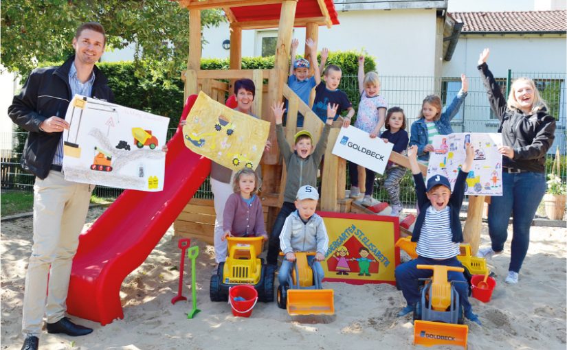 Einen kleinen Fuhrpark knallgelber Baufahrzeuge übergaben Maik Becker, Vertriebsingenieur bei Goldbeck Münster für die Region Osnabrück (links), und Verena Teigeler, Marketing der Niederlassung Münster (rechts), an die Leiterin der Kita St. Elisabeth, Sylke Otten (Mitte). Die Kinder, die aktuell in Notbetreuung sind, fahren die Sitzbagger, Sand-Sitzlader und LKW-Kipper schon mal ein. (Foto: Goldbeck Münster / Carsten Hinnah