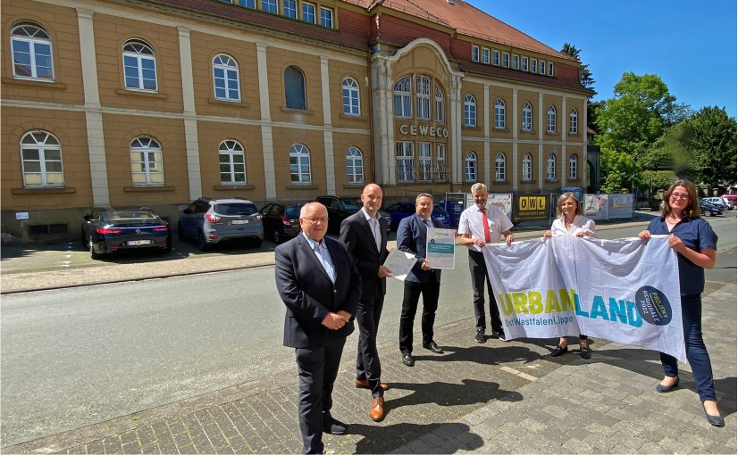 Dr. Axel Lehmann (3.v.l.) nahm REGIONALE-Urkunde und Fahne von Annette Nothnagel (2.v.r.) und den Förderbescheid von Jens Kronsbein (2.v.l.) entgegen. Dabei waren Investor Dieter Brechmann (links), Bürgermeister Dirk Becker (3.v.r.) sowie Marianne Petersmeier (rechts). Foto: OWL GmbH