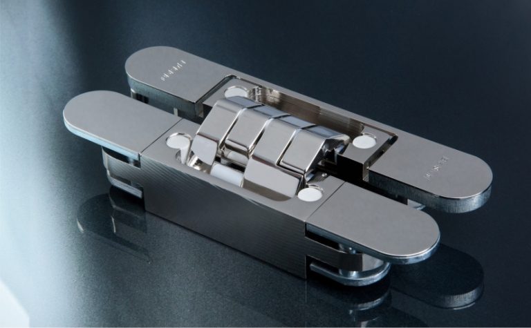 Das „Pivota DX 61 3-D“ in der Oberfläche poliert vernickelt: aktuelles Beispiel für ein verdeckt liegendes, dreidimensional justierbares Band für stumpf einschlagende Türen. In der „Design+“-Version decken magnetisch gehaltene Platten die Schraubenbereiche und die Ausfräsung in der Türzarge ab. Foto: BaSys