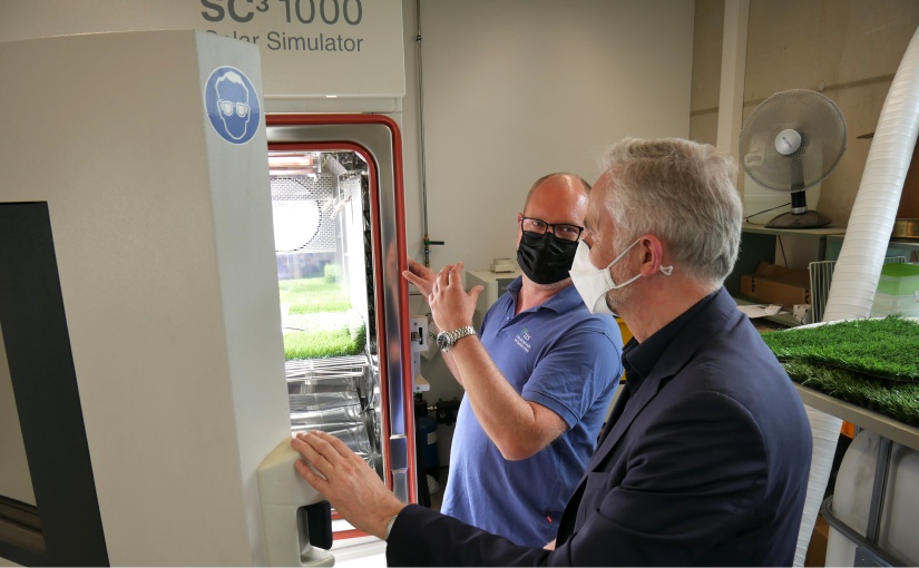 Geschäftsführer Oliver Schneider und Oberbürgermeister Wolfgang Griesert werfen einen Blick in den Solar-Simulator, in dem Kunstrasen auf Sonnentauglichkeit getestet wird. - Foto: WFO / Ingmar Bojes