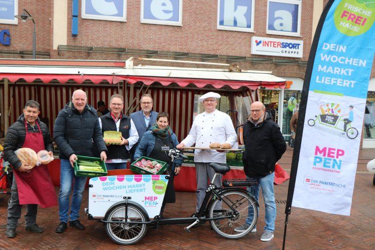 Christian Hüser, Freiwilligenzentrum Meppen des Paritätischen Emsland (2. v. l.), Bürgermeister Helmut Knurbein (Mitte) und Ansgar Limbeck, Geschäftsführer Stadtmarketingverein WiM e. V. (rechts), präsentieren gemeinsam mit den Wochenmarktbeschickern den neuen Lastenrad-Lieferservice (Foto: Stadt Meppen)