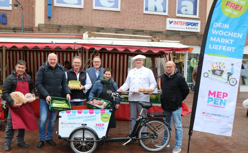 Christian Hüser, Freiwilligenzentrum Meppen des Paritätischen Emsland (2. v. l.), Bürgermeister Helmut Knurbein (Mitte) und Ansgar Limbeck, Geschäftsführer Stadtmarketingverein WiM e. V. (rechts), präsentieren gemeinsam mit den Wochenmarktbeschickern den neuen Lastenrad-Lieferservice (Foto: Stadt Meppen)