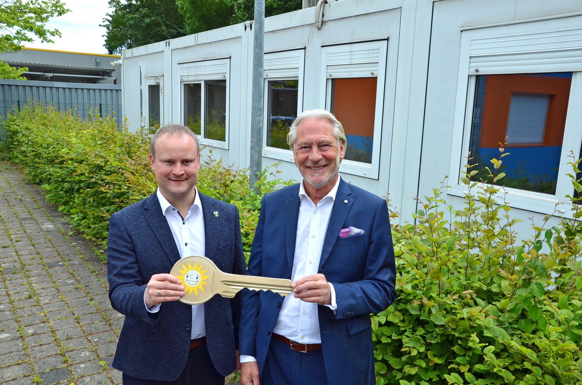 Jürgen Stühmeyer (rechts), Vorstand Merkur Vertrieb, übergibt den symbolischen Schlüssel für die Wohncontainer im Hintergrund an Espelkamps Bürgermeister Dr. Henning Vieker. (Foto: Gauselmann Gruppe)