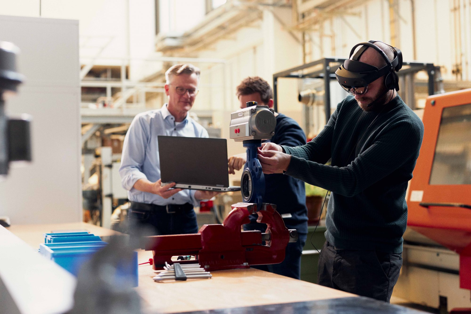 Projektmitarbeiter Lars Schalkwijk (3.v.l.) montiert mithilfe des mobilen Assistenzsystems „AVIKOM“ eine Absperrklappe. Über die Datenbrille und das Headset erhält er die entsprechenden Anweisungen. Besonders ist dabei, dass die Instruktionen individuell auf sein Vorwissen abgestimmt sind. (Foto: Patrick Pollmeier/FH Bielefeld)