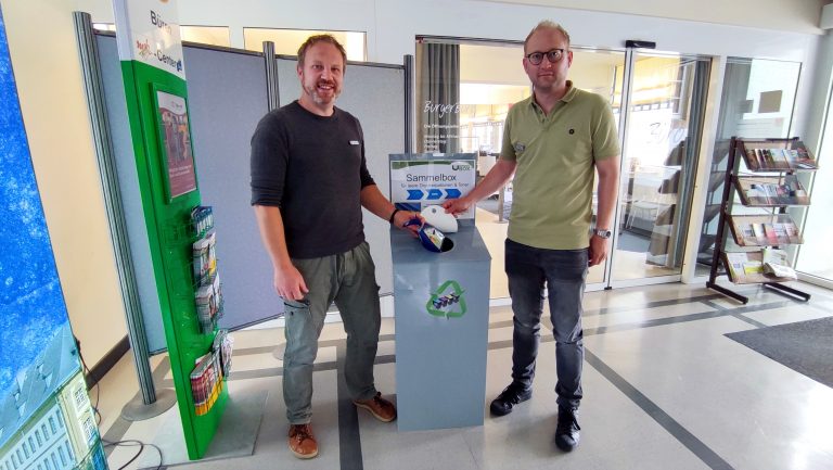 Manuel Krenz (Abteilungsleiter Bürgerdienste) und Sascha Glaser vor der Umweltbox im Bürgerbüro beim Einwerfen einer Druckerpatrone (Foto: Stadt Büren)