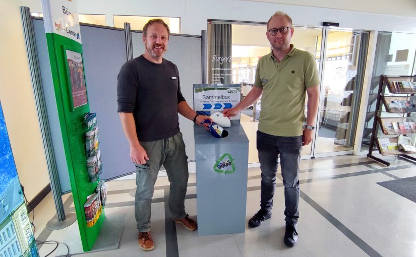 Manuel Krenz (Abteilungsleiter Bürgerdienste) und Sascha Glaser vor der Umweltbox im Bürgerbüro beim Einwerfen einer Druckerpatrone (Foto: Stadt Büren)