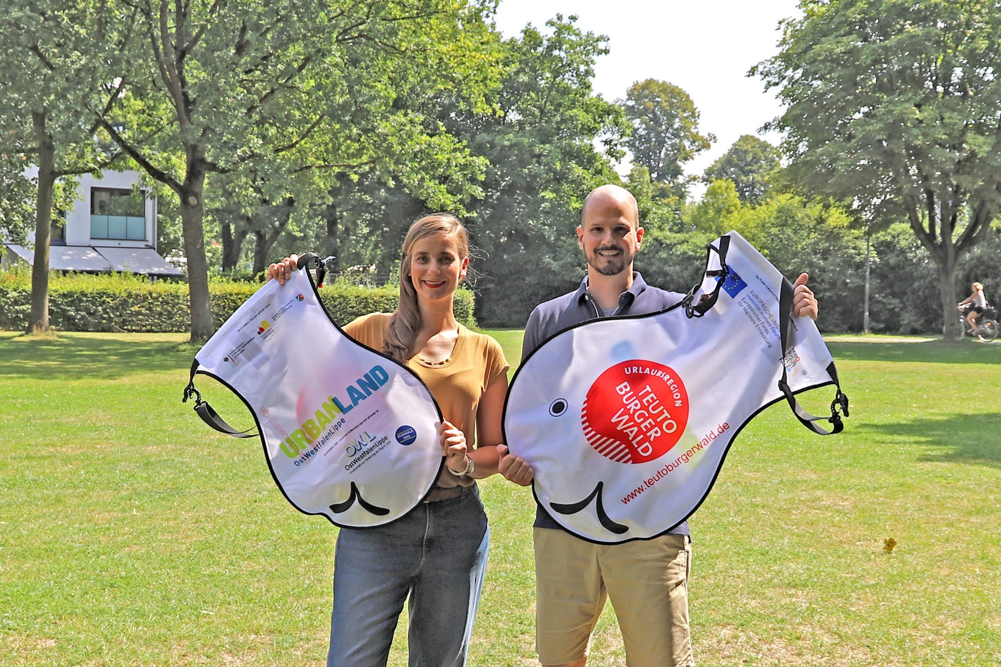 Melanie Adriaans, REGIONALE 2022, und Markus Backes, Teutoburger Wald Tourismus, stellen den Wickelfisch vor. Die OstWestfalenLippe GmbH unterstützt das 1. Mindener Weserschwimmen der DLRG mit 500 kostenfreien Wickelfischen. (Foto:OstWestfalenLippe GmbH)