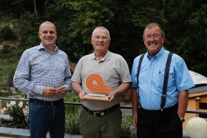 „In Dankbarkeit für 50 Jahre erfolgreiche Geschäftsbeziehung“ ist auf der Glasskulptur eingraviert, die trans-o-flex-CEO Wolfgang P. Albeck und der Geschäftsbereichsleiter Linienverkehr, Michael Zorell, dem Transportunternehmer Roman Mayer zum Jubiläum überreichen. (Foto: trans-o-flex)