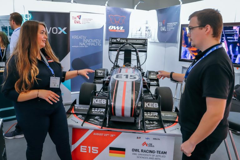 Ein Hingucker auf dem Messestand: Marlen Gausmann und Rober Cordie von der TH OWL vor dem Rennwagen des OWL Racing Teams, mit dem die TH OWL die Kompetenzen ihrer Studierenden in den Bereichen Entwicklung, Konstruktion und Fertigung präsentiert. (Foto: it’s OWL)