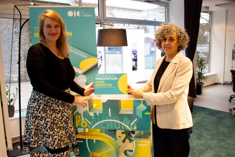 Almut Rademacher (links) und Maria Gonçalves präsentieren die druckfrische Ausgabe „Trendbuch Innovation – Open Industry“ im Innovation Office am Alter Markt 13 in der Bielefelder Altstadt. (Foto: Open Innovation City)