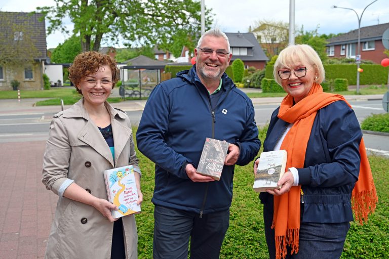 Natalia Neufeld (l.) und Maria Runde nahmen die Spende aus den Händen von Marcus Rüdiger entgegen. Mit einem Buch in der Hand zeigen die Drei schon einmal, wo der Bücherschrank aufge-stellt werden soll. (Foto: SWTE)