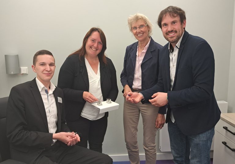 Er hat das perfekte Berufsfeld für sich gefunden: Hörgerä-teakustiker Christofer Macholla (links) erläutert gemeinsam mit Meisterin Kaya Harbaum-Salewski (2.v. links) Hildegard Hes-selbarth, ArbeitgeberService, und Michael Kelka, MaßArbeit-Bereichsleiter, die neuste Technik in Sachen Hörgeräte. (Foto: MaßArbeit / Kimberly Lübbersmann)