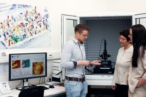 Weiß, wovon er redet: Julian Cremer ist wissenschaftlicher Mitarbeiter im Labor der Experimentalphysik und zeigt Prof. Dr. Sonja Schönung und Melanie Wilde (v.l.n.r.) wie ein Rasterkraftmikroskop arbeitet. Für seine Promotion führt er zahlreiche Experimente an dem Gerät durch. (Foto: P. Pollmeier/HSBI)