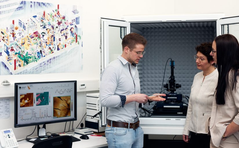 Weiß, wovon er redet: Julian Cremer ist wissenschaftlicher Mitarbeiter im Labor der Experimentalphysik und zeigt Prof. Dr. Sonja Schönung und Melanie Wilde (v.l.n.r.) wie ein Rasterkraftmikroskop arbeitet. Für seine Promotion führt er zahlreiche Experimente an dem Gerät durch. (Foto: P. Pollmeier/HSBI)