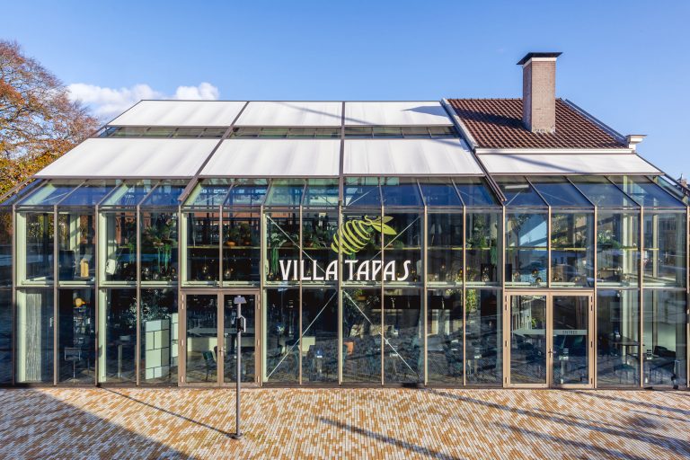 Das vollständig aus Glas gebaute Restaurant Villa Tapas im niederländischen Assen erhielt ein großflächiges Sonnenschutzsystem von Hersteller markilux. In der Kombination aus Aufglas- und Vertikalmarkisen ließ sich der Wärmeeintrag in das Gebäude deutlich reduzieren und damit Kühlenergie sparen. (Foto: markilux)
