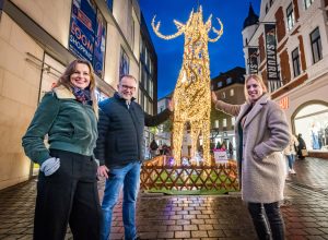 Birgit Schroers, Martin Knabenreich und Julia Lehmann (v. l.) von Bielefeld Marketing präsentieren das Lichtprojekt „Von hier wech“ am leuchtenden Hirsch an der Bahnhofstraße. (Foto: Bielefeld Marketing | Sarah Jonek)
