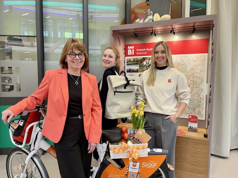 Gabriela Lamm, Jill Turner und Maya Regtmeier (v. l.) aus dem Tourismus-Team von Bielefeld Marketing stellen das Angebot für die Freizeitsaison 2025 vor. In der Tourist-Information in der Wissenswerkstadt bekommt man unter anderem auch den neuen BIE-Rucksack in den Farben Dunkelgrün, Beige und Schwarz. (Foto: Bielefeld Marketing)