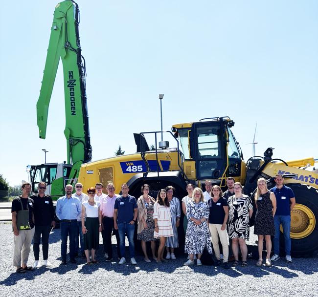 Gruppenfoto vor einer großen Baumaschine beim Nachhaltigkeitsnetzwerk-Treffen der WFL