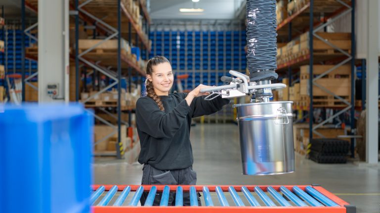 Mitarbeiterin bewegt ein Fass mit einem Vakuum-Schlauchheber in einer Lagerhalle