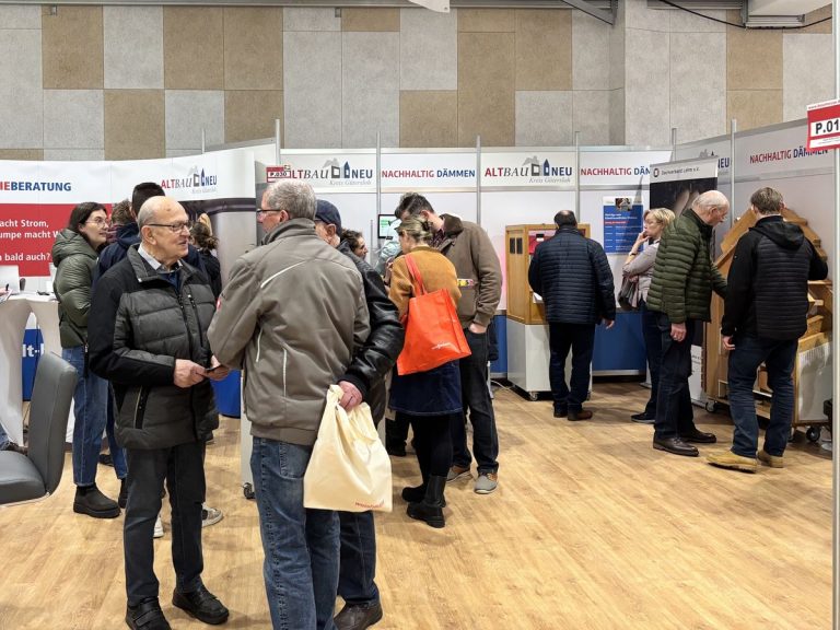 Besucherinnen und Besucher im Gespräch an einem Messestand der Initiative ALTBAUNEU auf der Baumesse Rheda-Wiedenbrück 2026