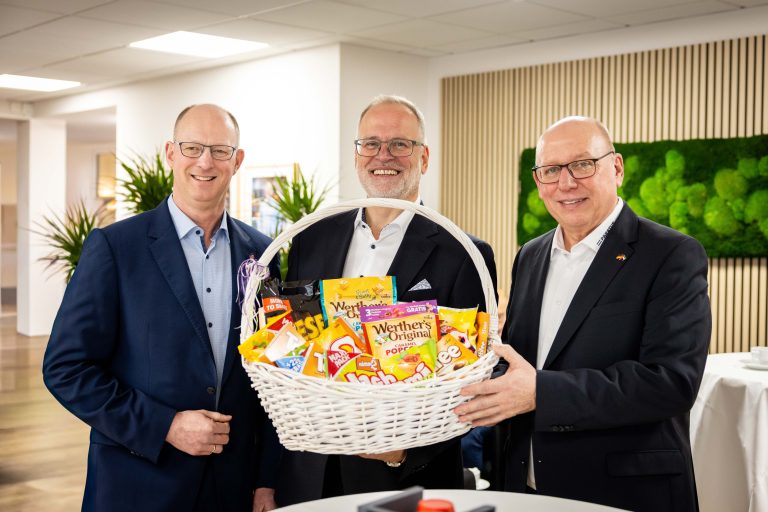 Zwei Gründer von SW-Paratus und der Bürgermeister von Halle (Westf.) halten einen Präsentkorb zur Einweihung der erweiterten Büroräume