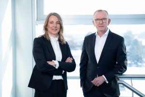 Natascha Sander (CFO) und Michael Finger (CEO) von technotrans stehen vor einem Fenster in einem Unternehmensgebäude