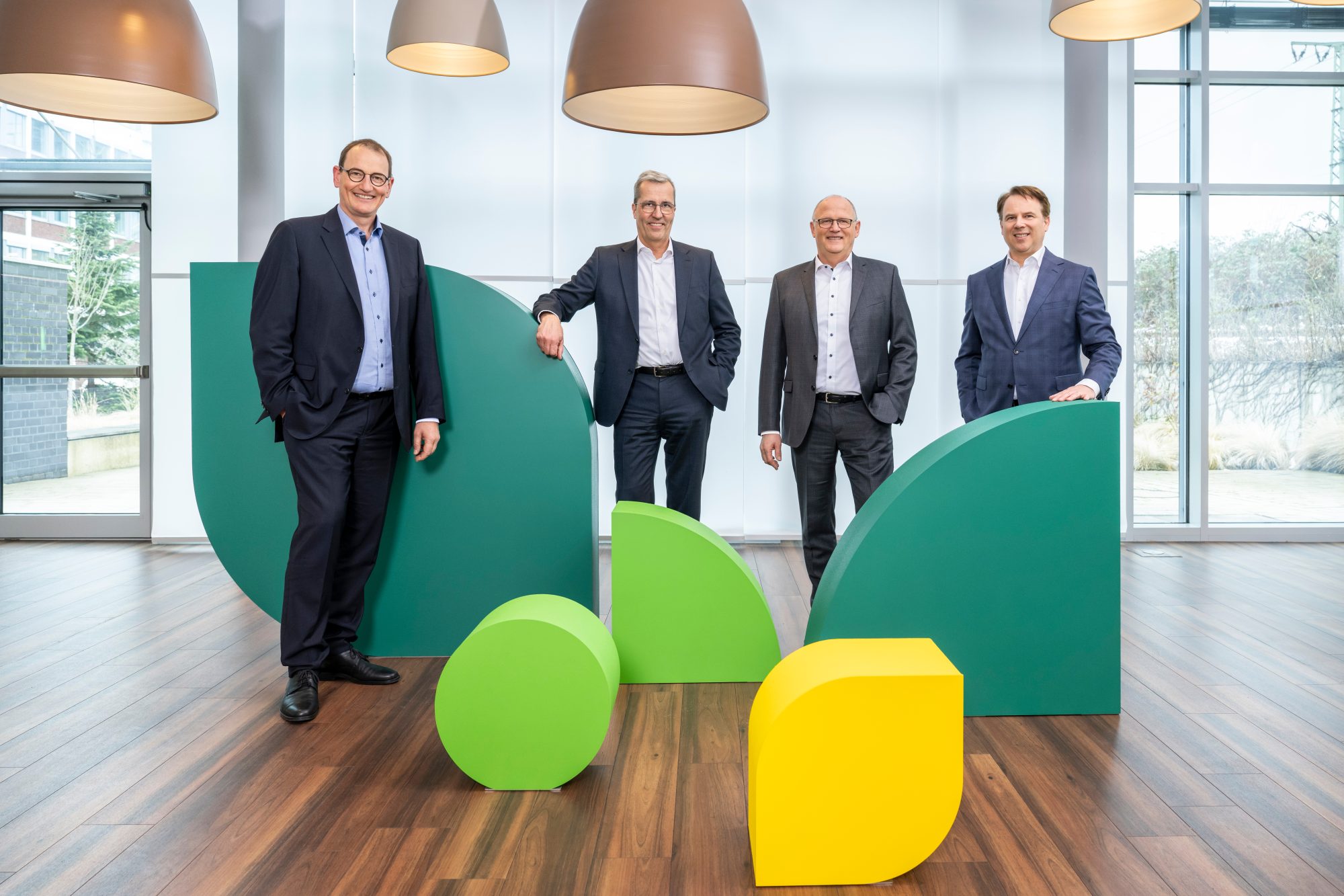 Vier Vorstandsmitglieder der AGRAVIS Raiffeisen AG stehen in einem hellen Unternehmensgebäude zwischen grün-gelben Gestaltungselementen.