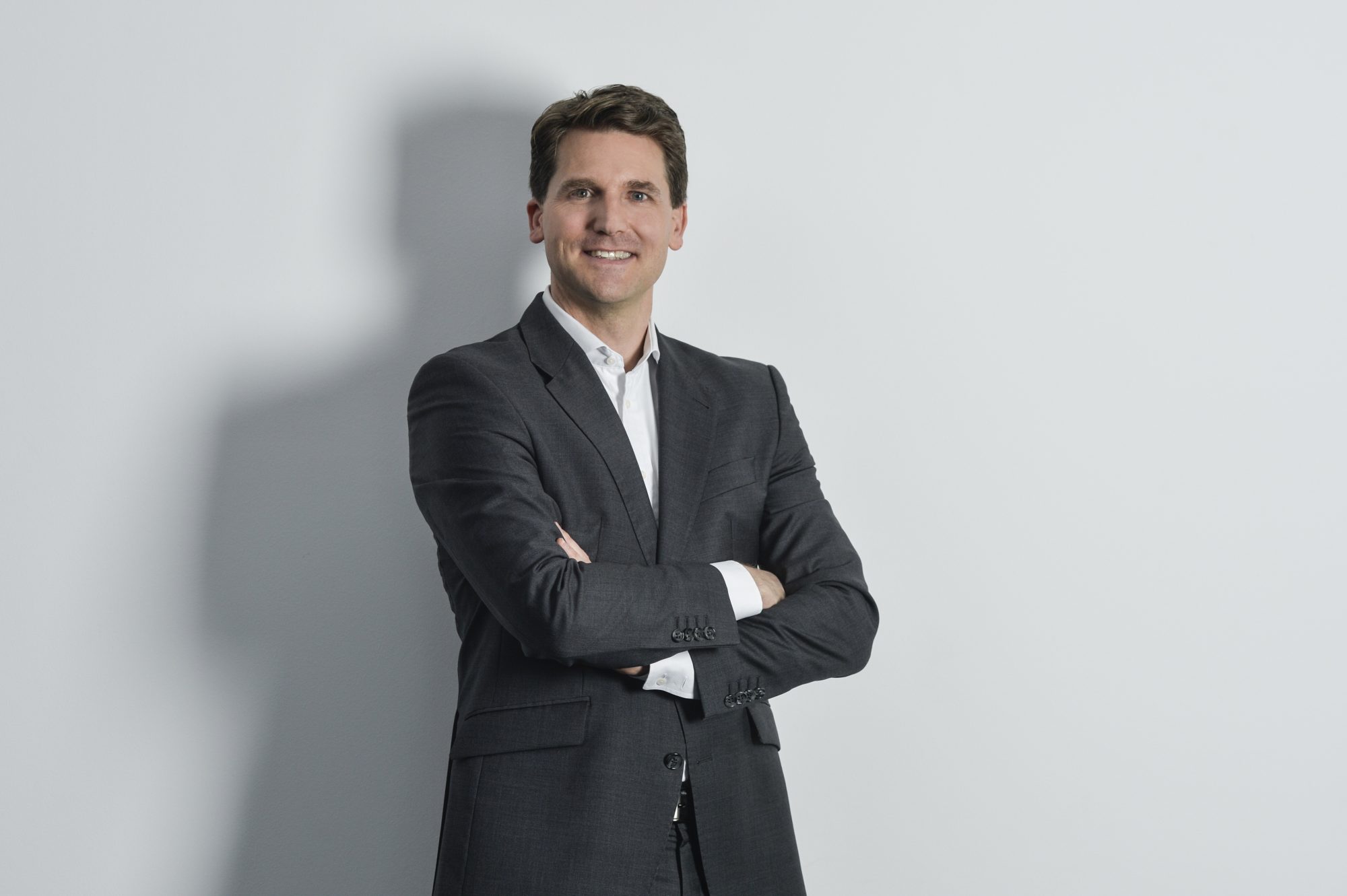 Porträt von Christian Hahn in dunklem Anzug vor grauer Wand, die Arme verschränkt.