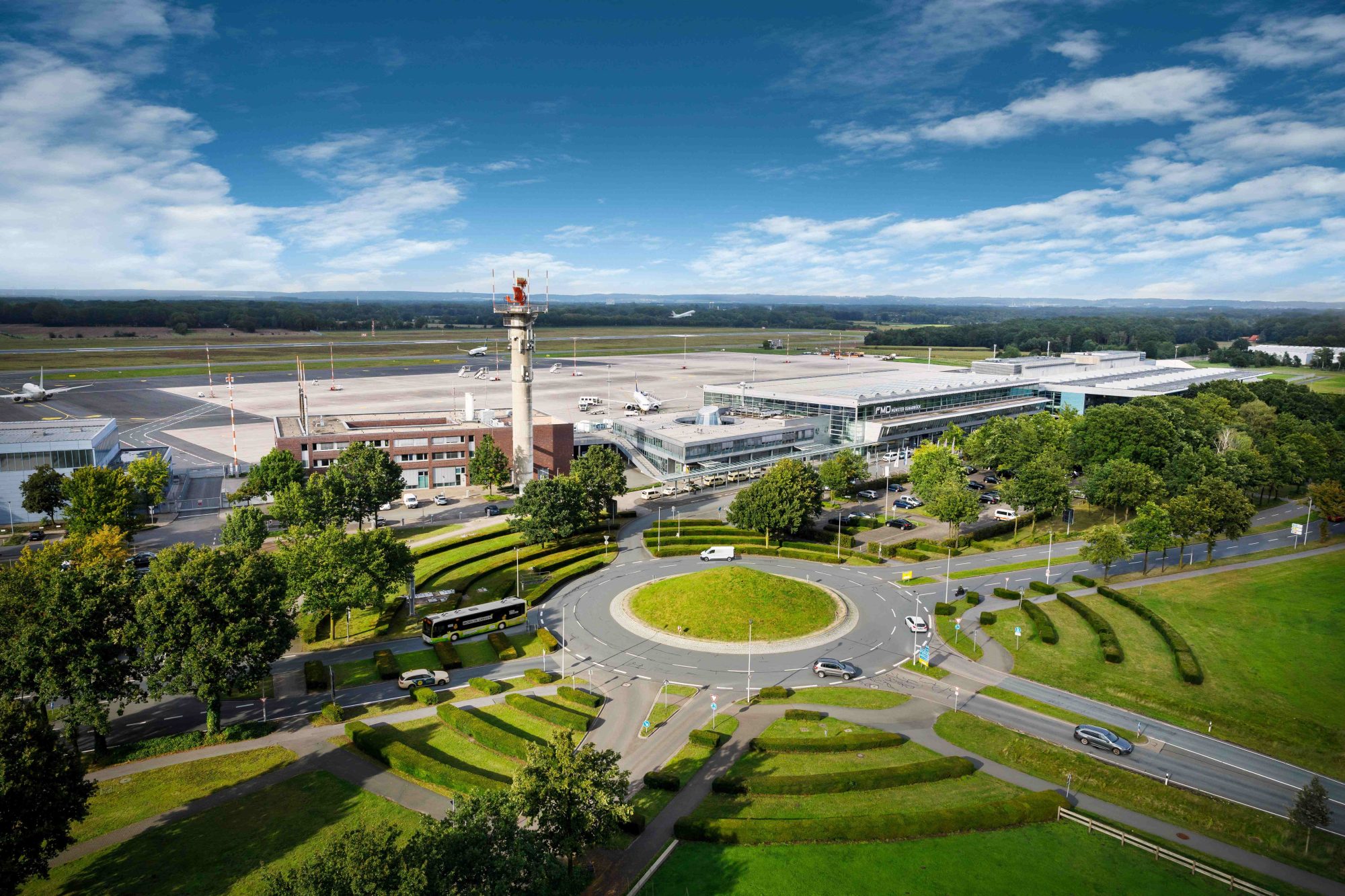 Luftaufnahme des Flughafens Münster/Osnabrück mit Terminal, Tower, Vorfeld und Kreisverkehr im Vordergrund.
