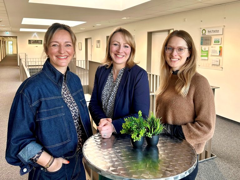 Sandra Schürmann, Frauke Barske und Carina Wolf stehen in einem Verwaltungsgebäude an einem Stehtisch und stellen das Modellprojekt für internationale Fachkräfte vor.