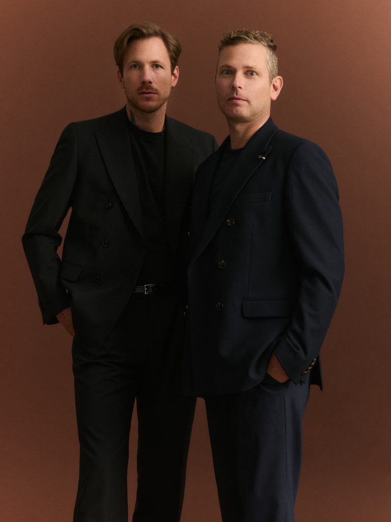 Julius Brinkmann und Markus Brinkmann von der bugatti Holding Brinkmann stehen vor braunem Hintergrund.