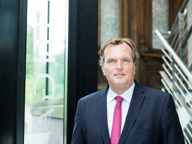 Dr. Jost Streitbörger im dunklen Anzug vor einer Glaswand in einem Bürogebäude