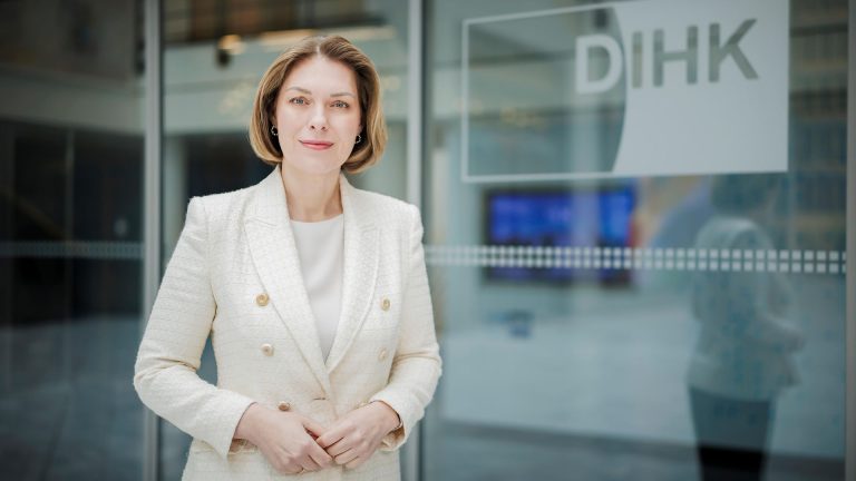 DIHK-Hauptgeschäftsführerin Helena Melnikov in einem weißen Blazer vor einer Glaswand mit DIHK-Logo