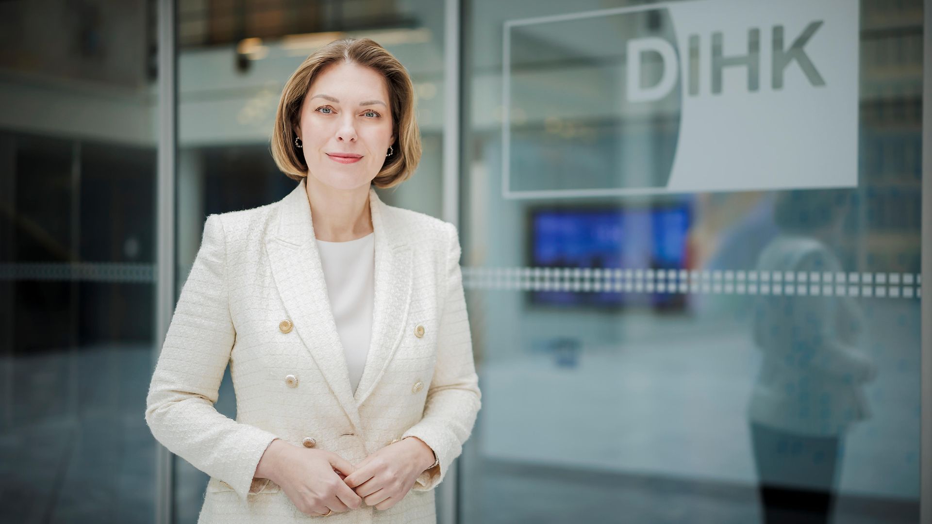 DIHK-Hauptgeschäftsführerin Helena Melnikov in einem weißen Blazer vor einer Glaswand mit DIHK-Logo