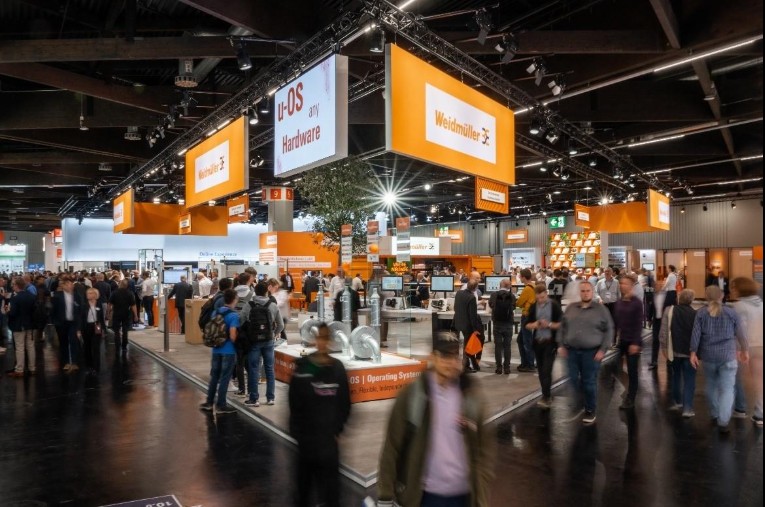 Besucher am Weidmüller-Messestand mit orangefarbenen Standaufbauten; Archivbild.