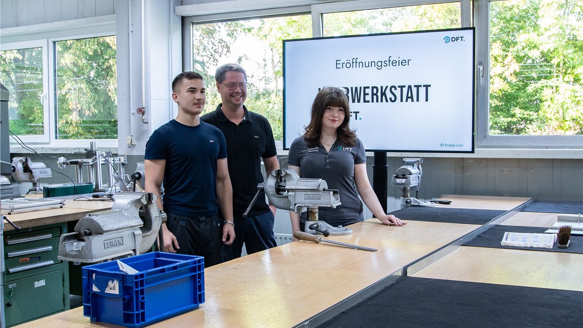 Drei Personen an Werkbänken mit Schraubstöcken in der DFT-Lehrwerkstatt.