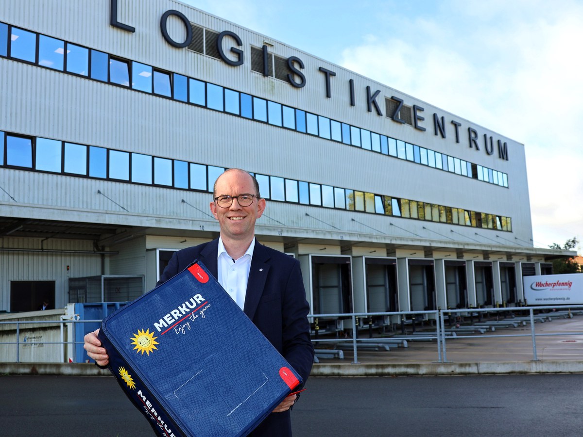 Philipp Obermark mit einer blauen Merkur-Mehrwegbox vor dem Logistikzentrum